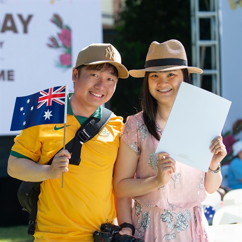 Two people holding an Australian flag and citizenship certificate