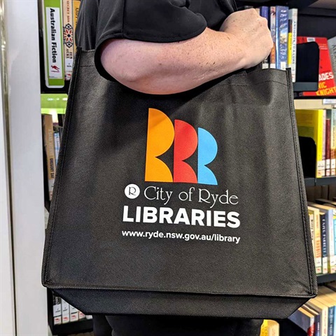 Person holding a library bag over their shoulder with bookshelves in the background