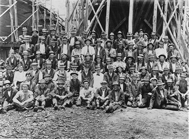 Shipyard workers, Kidman & Mayoh, Putney, January 1920.  Kidman & Mayoh were contracted to build wooden ships as steel was difficult to obtain during WWI. The workforce included a few skilled shipwrights, bush carpenters and timber workers from the North Coast of NSW. Some local Putney people got jobs as blacksmith & labourers.  Ryde Library Service. Acc. 4796497. Kidman & Mayoh Shipyard / 5