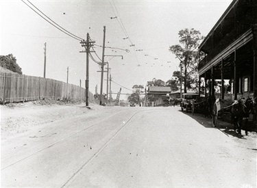Looking west at the level crossing at West Ryde, 5 February 1935. The original way to cross the railway line at Ryde Railway Station (now West Ryde Railway Station) was via a level crossing. Initially this was controlled with swing gates that had to be manually opened and closed; later the gates were controlled from the signal box. Visible in his photo are the tram tracks for the extension from Hatton’s Flat and, on the extreme right, the Royal Hotel which was demolished in the 1930s. Ryde District Historical Society. Image 3913; negative 157/10.