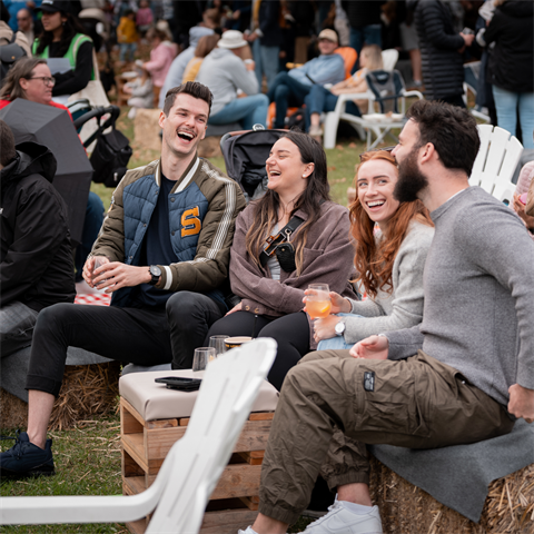 Group of four laugh and enjoy drinks amongst a large outdoor crowd