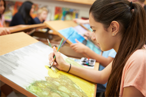 Girl sits a desk painting a landscape picture