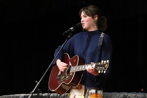 Young lady playing guitar and singing on stage