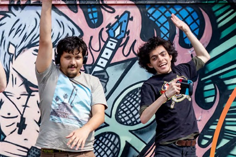 Two young men dancing in front of wall mural