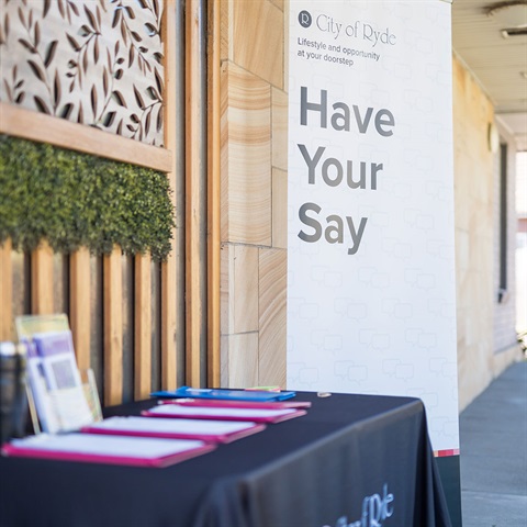 Table with clipboards and flyers, next to a banner that says Have Your Say.