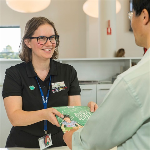 Woman handing man book at library