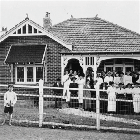 Boy alone and crowd of women pose in front of a house
