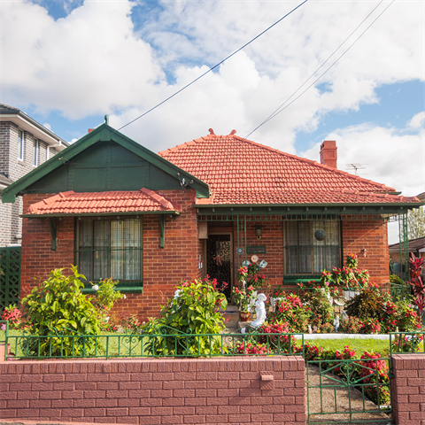 Front view of a red brick house, flower gardens, and front brick fence with a low green gate