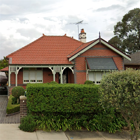 Front view of a single-storey red brick house, set behind a wide hedge and tree