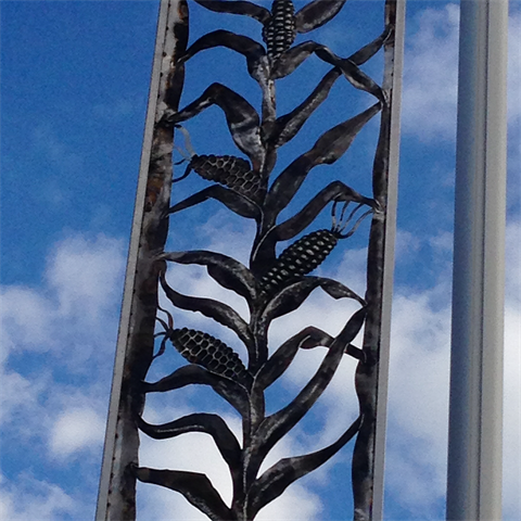 Detail view of an iron sculpture of a corn plant with the blue sky behind it