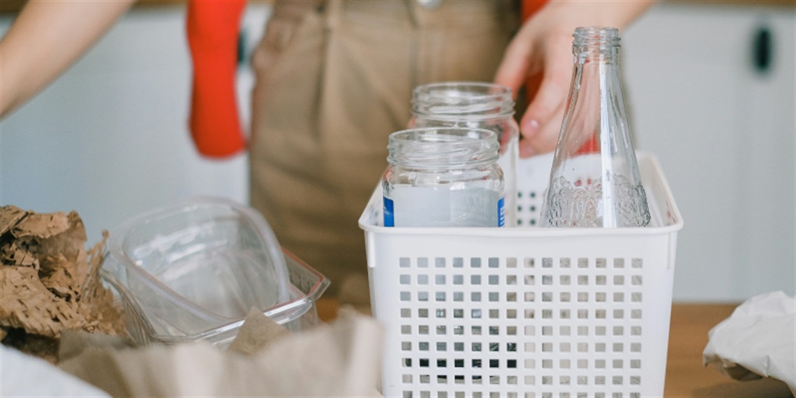 Photo of a glass bottles in a basket surrounded by recycling materials