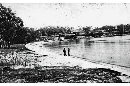 Old black and white photo of Putney Beach, two people stand by the shore