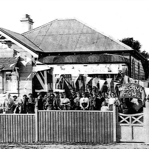 Crowd of people stand behind a fenced off house
