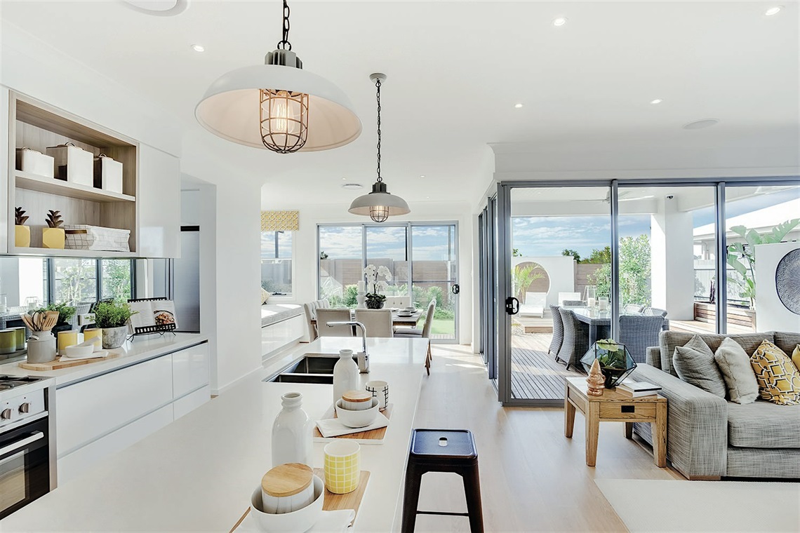 View of the interior of a house, including the kitchen, lounge room, and dining room, with windows overlooking the back yard