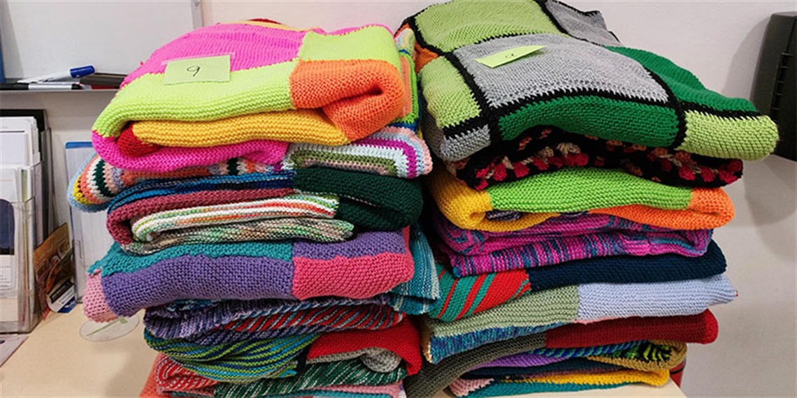 Two piles of colourful hand knitted blankets